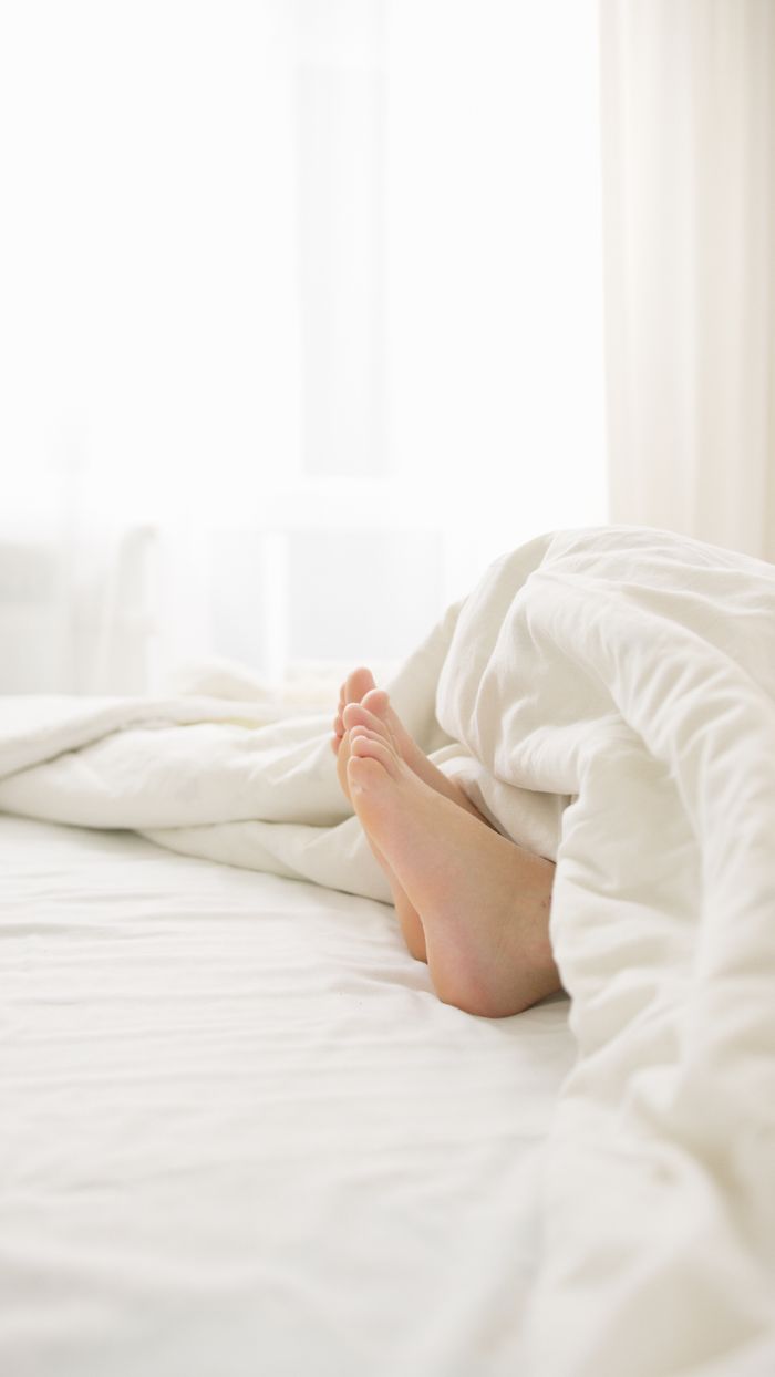 Bare feet peek out from under a white comforter, evoking a sense of warmth and relaxation.